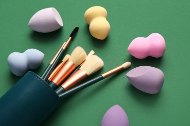 Yeşil arkaplanda makyaj süngerleri ve fırçalar