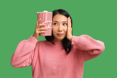 Yeşil arka planda patlamış mısır kovası olan genç Asyalı kadın.