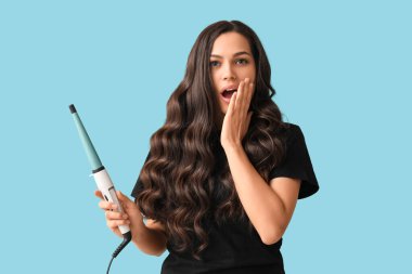 Mavi arka planda saç maşasıyla şaşırmış genç bir kadın.