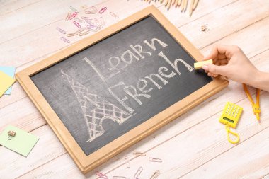 Kadın eli, yazı tahtası LEARN FRENCH ve hafif ahşap zemin üzerinde farklı kırtasiye malzemesi, yakın plan