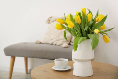 Oturma odasındaki sehpanın üzerinde minderleri ve vazo dolusu sarı laleleri olan rahat bir bank.