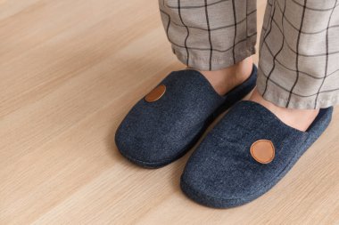 Erkek bacakları sıcak mavi terlikler içinde lamine zeminde, yakın plan.