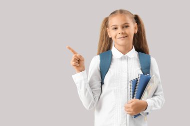 Not defterleri ve kalem kutusuyla gri arka plandaki bir şeyi gösteren okul üniformalı şirin küçük bir kız.