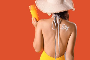 Şapkalı genç bir kadın, güneş kreminden yapılmış kelime ile turuncu arka plan, arka plan