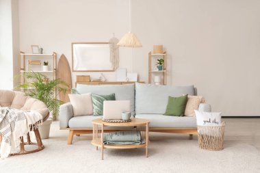 Pencerenin yanındaki sehpanın üzerinde gri kanepe ve modern dizüstü bilgisayarla aydınlık oturma odasının içinde.