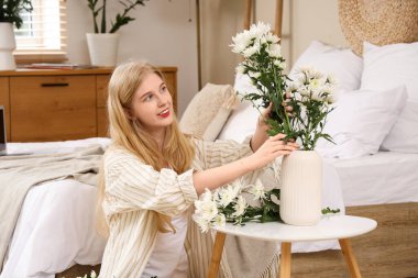 Güzel, genç, mutlu bir kadın vazoya bir buket beyaz kasımpatı koyuyor.