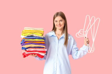 Pembe arka planda bir sürü renkli elbisesi ve askısı olan genç bir kadın.