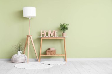 Pouf, yer lambası ve yeşil duvarın yanındaki masa.