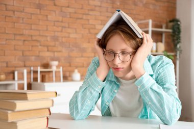 Evde kitapla gözlüklü yorgun bir erkek öğrenci.