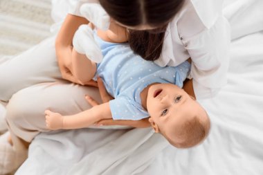 Güzel, genç Asyalı bir anne ve tatlı küçük bebeği evde, yatakta oturuyor, yakın plan.