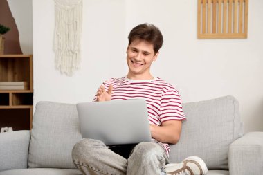 Genç adam evdeki kanepede dizüstü bilgisayarla görüntülü sohbet ediyor.