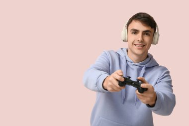 Kulaklıklı yakışıklı genç adam pembe arka planda video oyunları oynuyor.