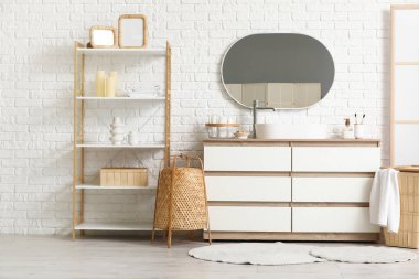 Banyonun içindeki beyaz tuğla duvarın yanında sandık ve raf ünitesi var.