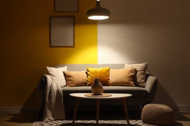 Gri kanepesi, masası ve parlayan lambası olan karanlık oturma odasının içinde.