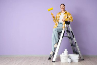 Leylak duvarının yanındaki merdivende boya silindirli genç bir kadın.