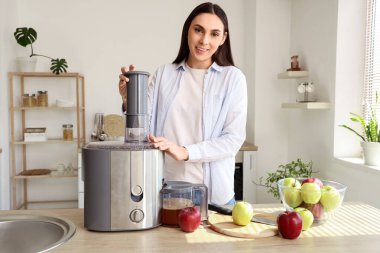 Modern meyve sıkacağı ve mutfaktaki masada elmaları olan genç bir kadın.