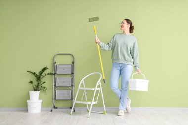 Yeşil duvarın yanında merdiveni ve boyası olan genç bir kadın.