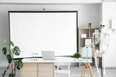 Masada insan iskeleti modeli, projektör ekranı ve modern dizüstü bilgisayarı olan hafif bir hastane.