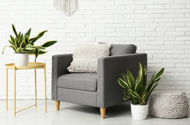 Beyaz tuğla duvarın yanında koltuk, puf, masa ve sansevieria bitkileriyle dolu bir oda.