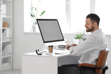 Boş bilgisayarlı genç işadamı masada akıllı adamı kontrol ediyor.