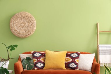 Oturma odasındaki yeşil duvarın yanında yastıkları olan rahat kahverengi kanepe.