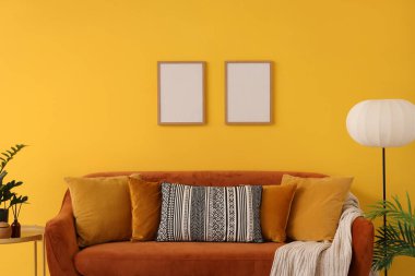 Oturma odasındaki sarı duvarın yanında yastıklı ve ekoseli rahat kahverengi kanepe.