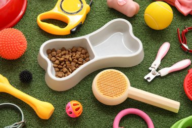 Kemik şeklinde yemek kasesi ve yeşil çimenlerin üzerinde farklı hayvan aksesuarları.