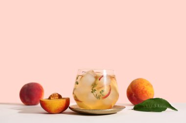 Bir bardak taze şeftalili limonata kekik ve bej arka planda beyaz masada meyveler.