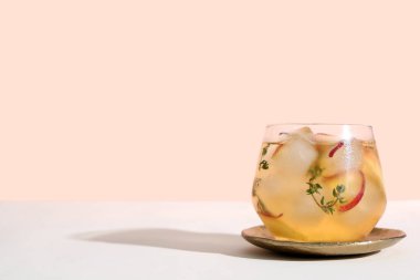 Bir bardak taze şeftalili limonata ve bej arka planda beyaz masada kekik.