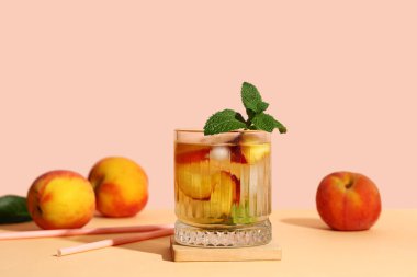 Bir bardak taze şeftalili limonata ve turuncu masada bej arka planda meyveler.