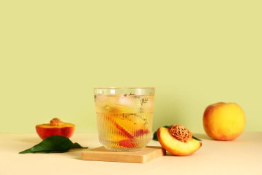 Bir bardak taze şeftalili limonata ve yeşil arka planda bej masadaki kekik.