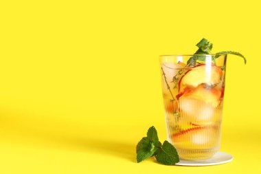 Bir bardak taze şeftalili limonata, sarı arka planda nane şekeri.