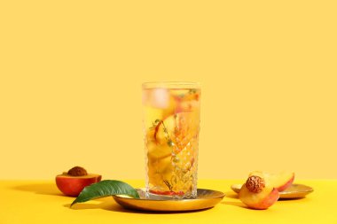 Sarı arka planda kekik olan bir bardak taze şeftalili limonata.