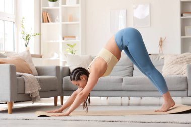 Rastalı genç bir kadın evde yoga yapıyor.
