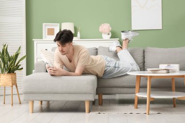 Evdeki gri koltukta cep telefonu kullanan genç adam.