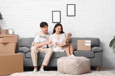 Genç çift evdeki kanepede paket kutusunu açıyor.