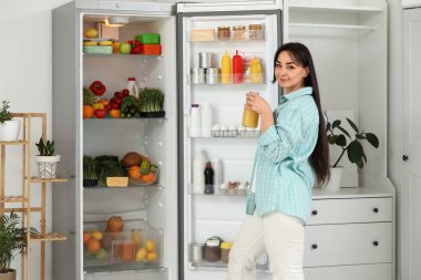 Mutfaktaki açık buzdolabının yanında meyve suyu olan güzel bir kadın.