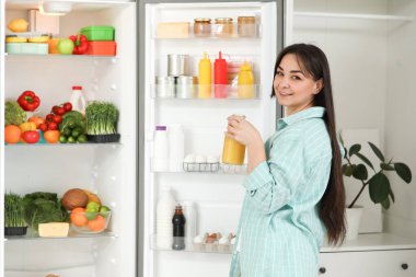 Mutfaktaki açık buzdolabının yanında meyve suyu olan güzel bir kadın.