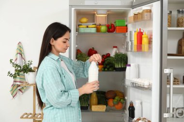 Mutfaktaki açık buzdolabının yanında bir şişe sütle güzel bir kadın.