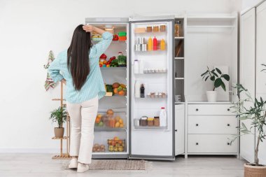 Mutfaktaki açık buzdolabının yanında düşünceli bir kadın.