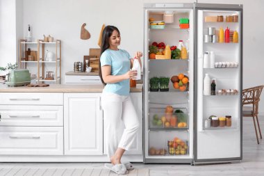 Mutfaktaki açık buzdolabının yanında yoğurtlu güzel bir kadın.