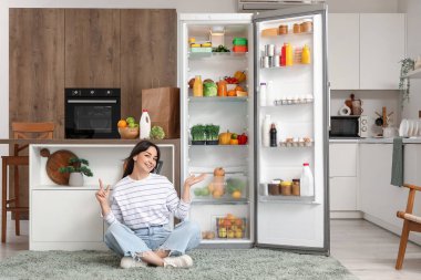 Güzel bir kadın mutfaktaki açık buzdolabının yanındaki bir şeyi işaret ediyor.