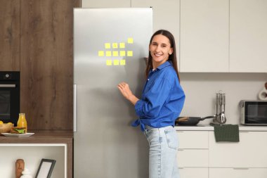 Mutfaktaki buzdolabına yapışkan notlar bırakmış genç bir kadın.