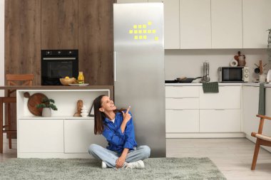 Mutfaktaki buzdolabını gösteren genç bir kadın.