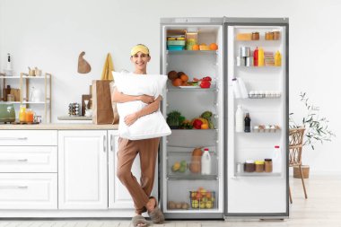 Mutfaktaki açık buzdolabının yanında yastıklı genç bir kadın.