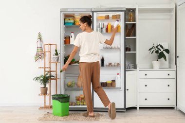 Mutfaktaki açık buzdolabından bozuk yemek atan genç bir kadın.