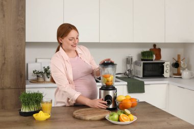 Genç hamile bir kadın mutfakta turunçgillerle meyve suyu yapıyor.