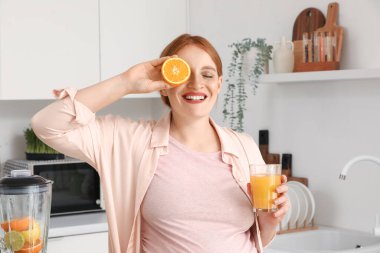Mutfakta portakal suyu ve bir bardak meyve suyu olan hamile bir kadın.