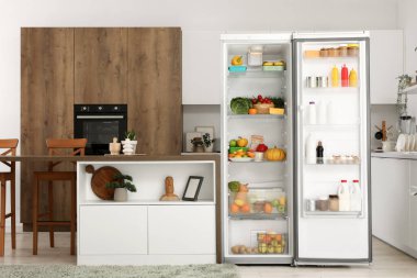 Açık buzdolabı, masa ve ürünleri olan mutfağın içi.