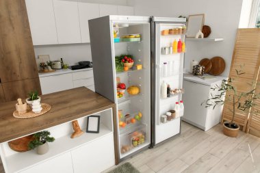 Açık buzdolabı, masa ve ürünleri olan mutfağın içi.